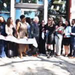 people stand in front of building while ribbon is being cut