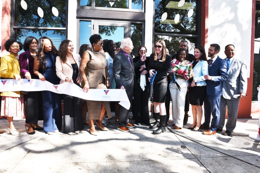 people stand in front of building while ribbon is being cut